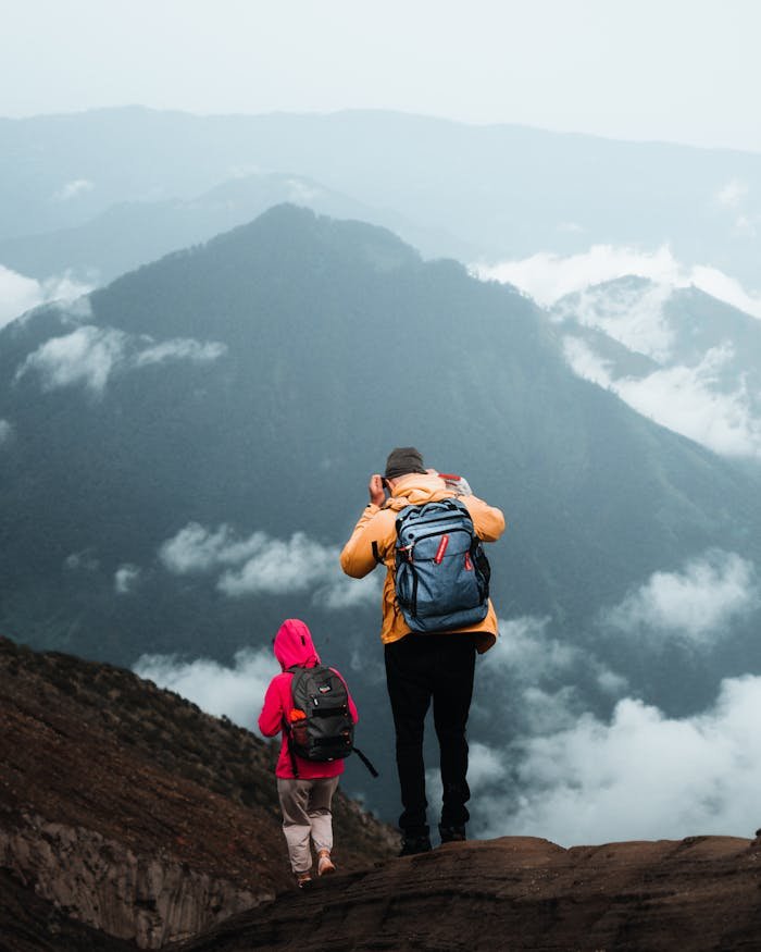 services-04 Two hikers enjoy a breathtaking view of Indonesian mountains shrouded in clouds, capturing the essence of adventure.