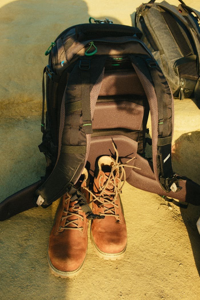 our-story A backpack and boots arranged on a sandy surface, perfect for travel or adventure themes.