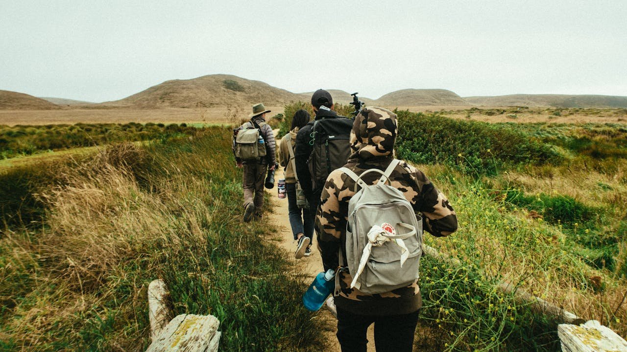A group of hikers walking along a scenic trail through grassy and mountainous terrain.